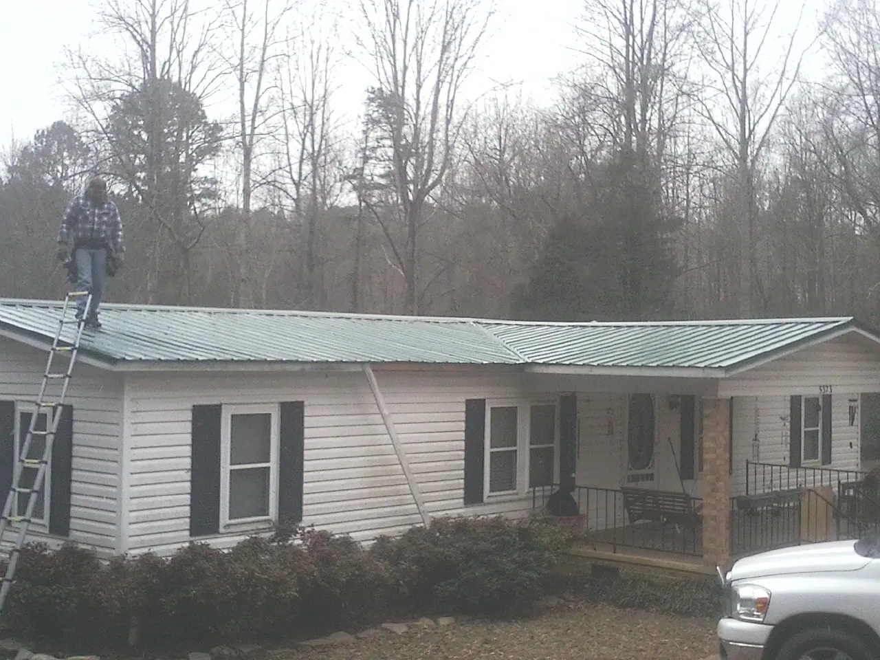 Worker on a ladder beside a new green metal roof on a ranch home in Waterford Works