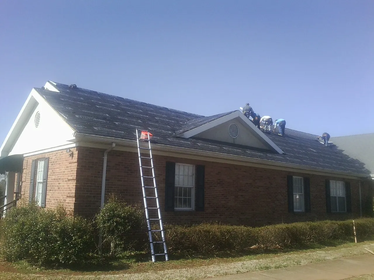Crew tearing shingles off a brick ranch roof with a ladder set — Metal Roof Repair work by our crew in Waterford Works