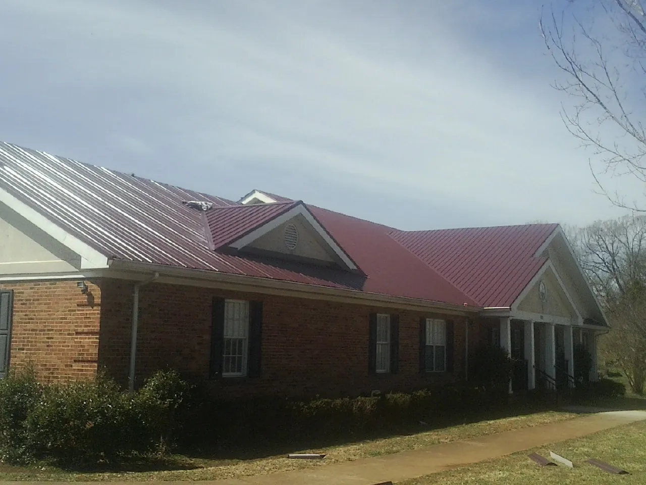 Red metal roof with gabled entries on a long brick building, from a Hail Damage Roof Repair job in Waterford Works
