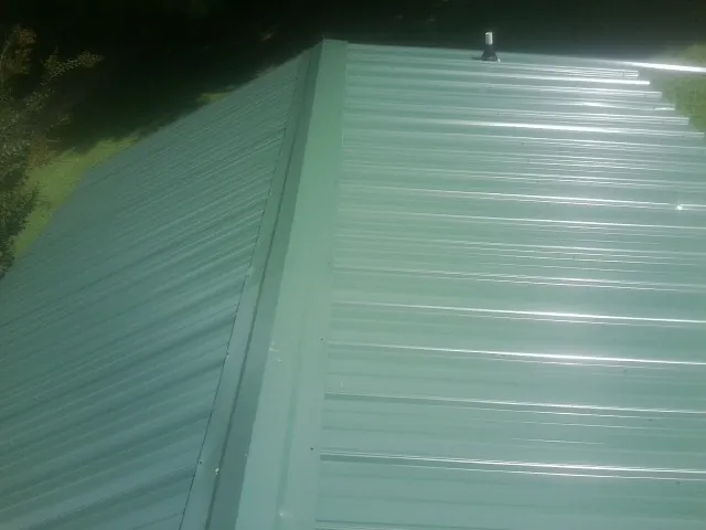New green metal panels meeting at the ridge of a roof — Flat Roof Repair work by our crew in Waterford Works