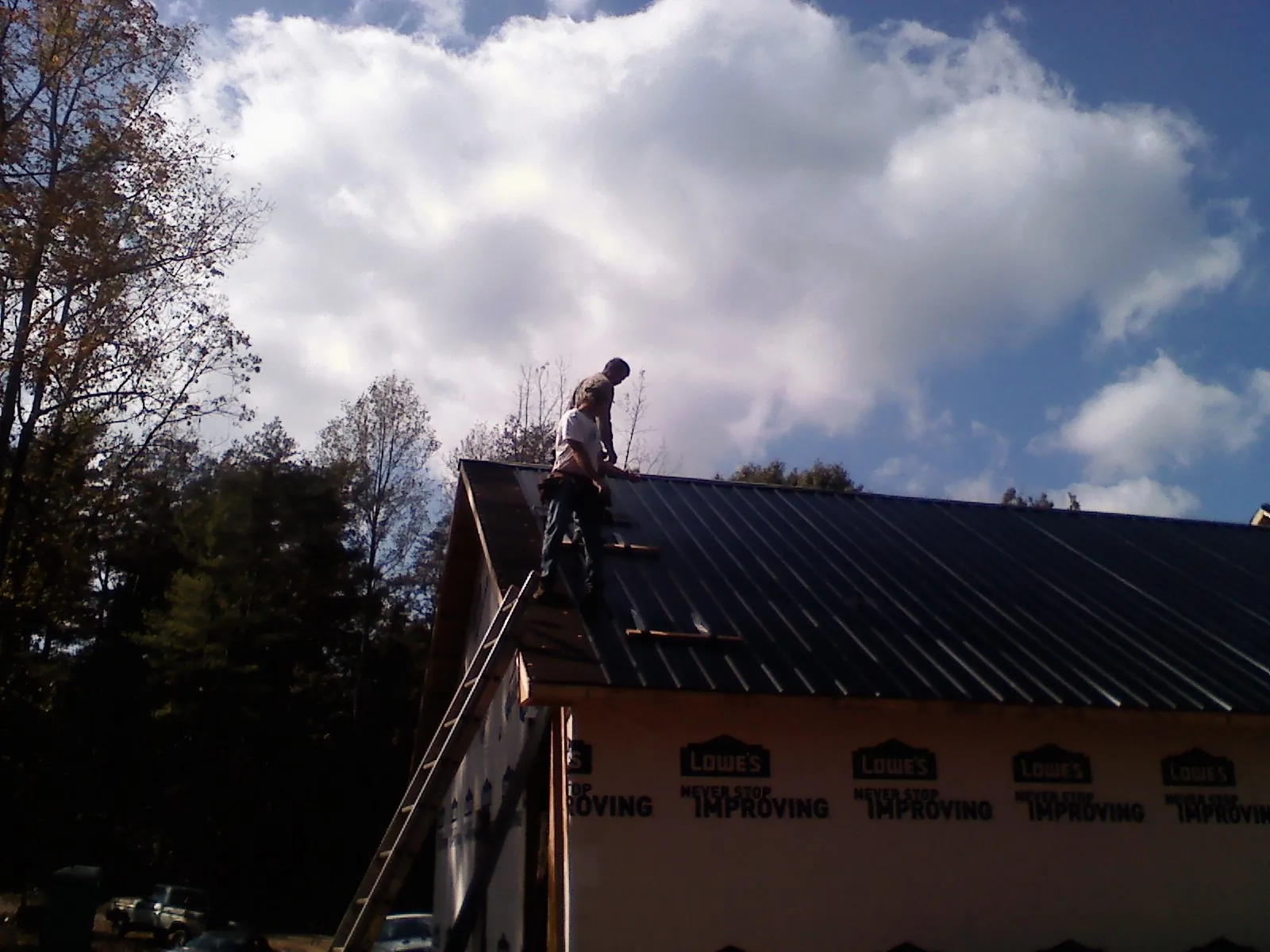 Roofer fastening dark metal panels high against a cloudy sky, from a Roof Inspection job in Waterford Works