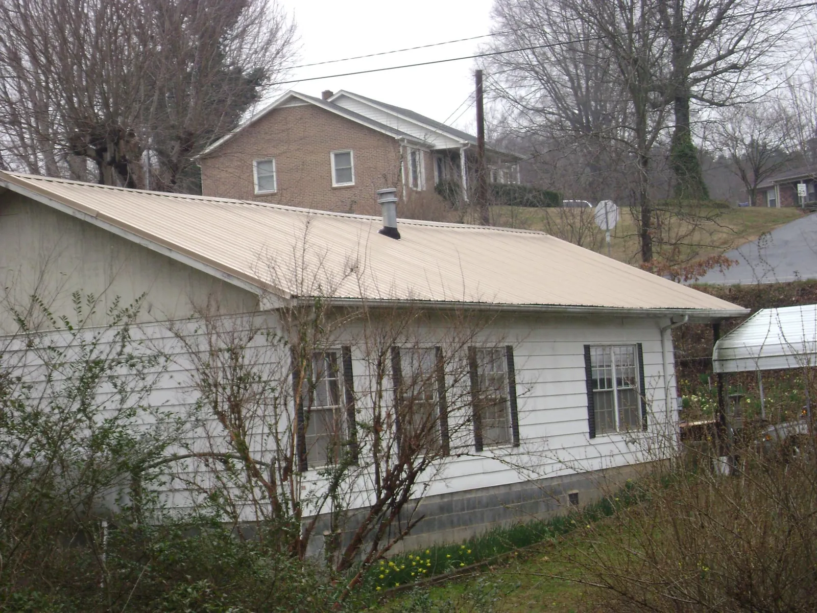 Tan metal roof on a white sided house set into a hillside — Commercial Roofing by Roofing Brothers in Waterford Works